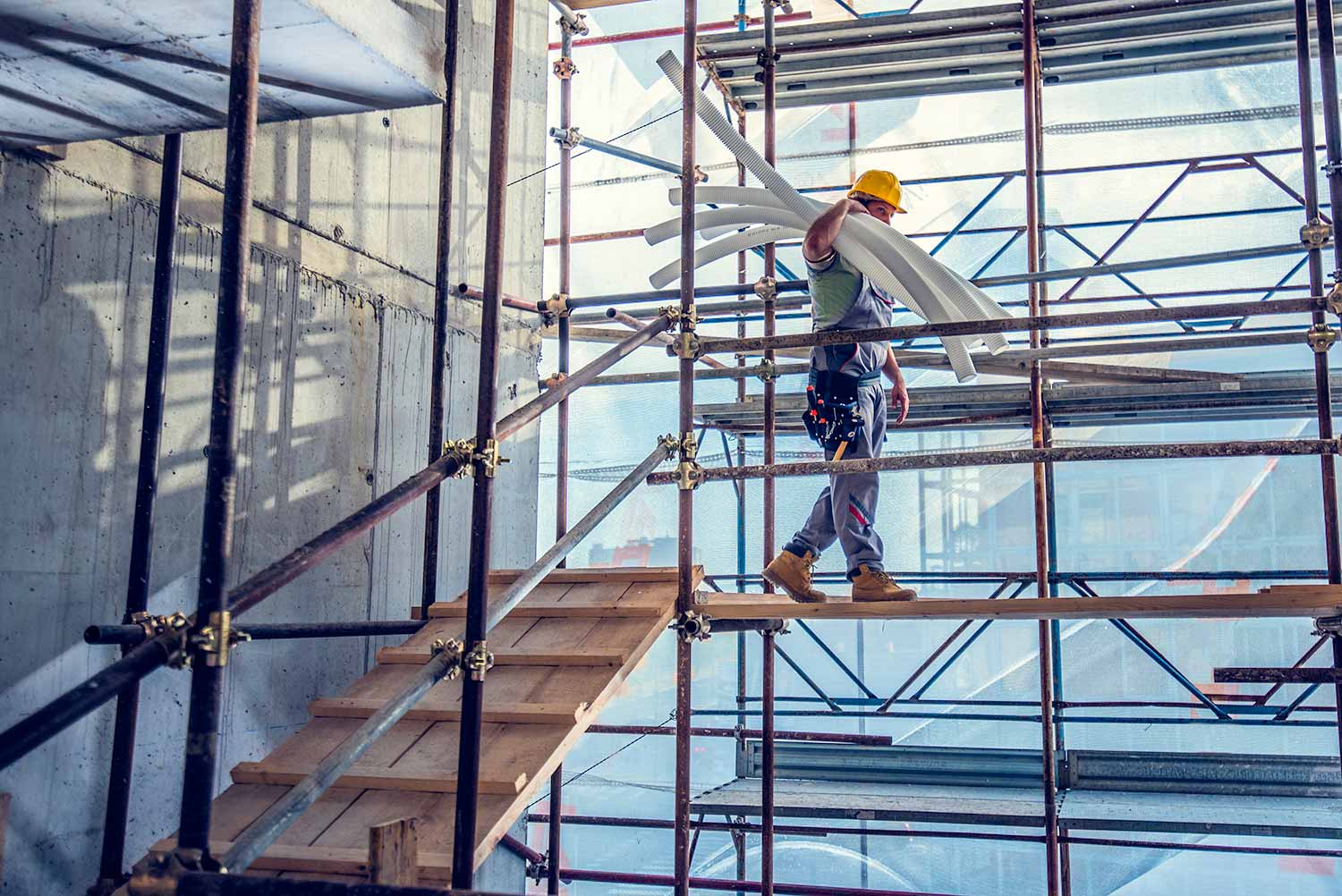 Worker carrying flexible conduit across a scaffold platform inside a building under construction