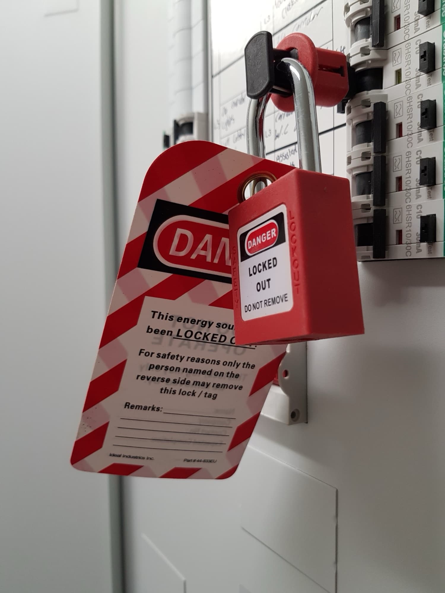 Red lockout padlock and a Danger Locked Out tag securing a circuit breaker on an electrical distribution panel