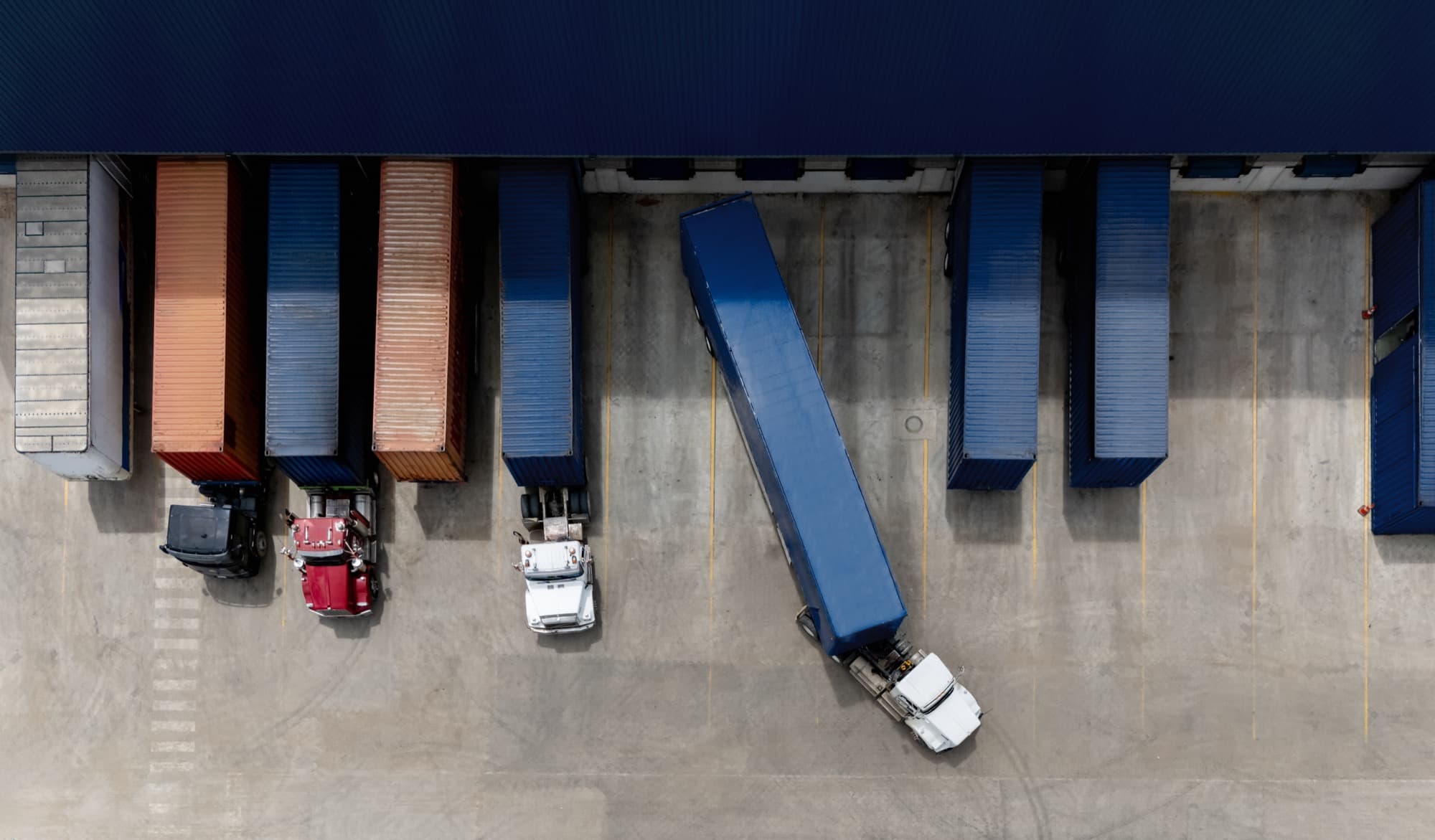 Aerial view of tractor-trailers at distribution-center loading docks while one truck maneuvers through the yard.